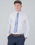 Man wearing dusty blue silk tie with white dress shirt and dark trousers against plain background