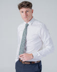 Man wearing a white shirt and brown belt with a forest green cotton tie featuring a floral William Morris "Clover" pattern.