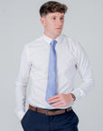 Man wearing a dusty blue silk tie paired with a white shirt and navy trousers against a plain background