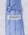 Close-up of dusty blue silk tie with Crossrow London label on smooth textured fabric.