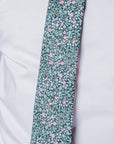 Close-up of Clover Grove cotton tie with intricate red and white floral pattern on deep green background worn with white shirt.