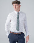 Man wearing white shirt and navy trousers styled with a deep green Clover Grove cotton tie featuring a botanical pattern