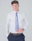 Man wearing dusty blue silk tie with white dress shirt and navy trousers on light background