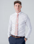 Man wearing a white shirt and navy pants with the floral patterned Cotswold Bloom tie in pink, orange, and yellow tones.