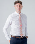 Man wearing a white shirt and Cotswold Bloom tie with floral pattern in pink, orange, and yellow on beige background
