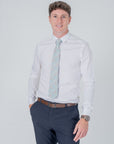 Man wearing Golden Lily Sage cotton tie with floral pattern, white shirt, navy pants, and brown belt against white background