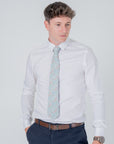 Man wearing white shirt and navy pants with a Golden Lily Sage cotton tie featuring floral botanical patterns