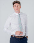 Man wearing a white shirt and navy trousers with a Golden Lily Sage cotton tie featuring floral botanical patterns.