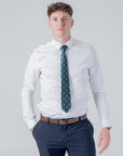 Man wearing a green polyester tie with gold skull crest pattern styled with white shirt and navy pants