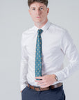 Man wearing a green polyester tie with gold skull and crossbones pattern paired with white shirt and navy pants