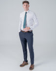 Man wearing white shirt and navy pants with green and gold skull crest polyester tie standing against gray background