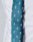 Close-up of a green polyester tie with gold skull and crossbones pattern, worn with a white dress shirt.
