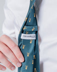 Close-up of green polyester tie with gold skull crest pattern and Crossrow London label on a white shirt