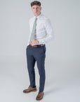 Man wearing Elmwood Bloom cotton tie with floral pattern, white shirt, navy pants, and brown shoes in a studio setting