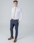 Man wearing amberwild bloom cotton tie with orange and yellow floral pattern on pale background, white shirt, navy pants