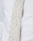 Close-up of a cotton tie with orange, yellow blossoms, and green foliage on a pale background worn with a white shirt.