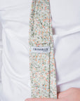 Close-up of Amberwild Bloom Cotton Tie with delicate orange and yellow blossoms on pale backdrop worn with white shirt