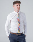 Man wearing a colorful Camden Block Check Tie with ochre, rust, sage, and blue hues, paired with a white shirt and navy pants.
