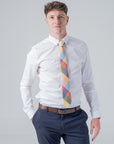 Man wearing a white shirt and Camden Block check tie with ochre, rust, sage, and blue patchwork design.
