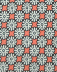 Close-up of Coral Bloom polyester tie fabric with white floral motifs and coral-red geometric accents on grey background.