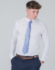 Man wearing a dusty blue silk tie with a white shirt and dark trousers against a plain background