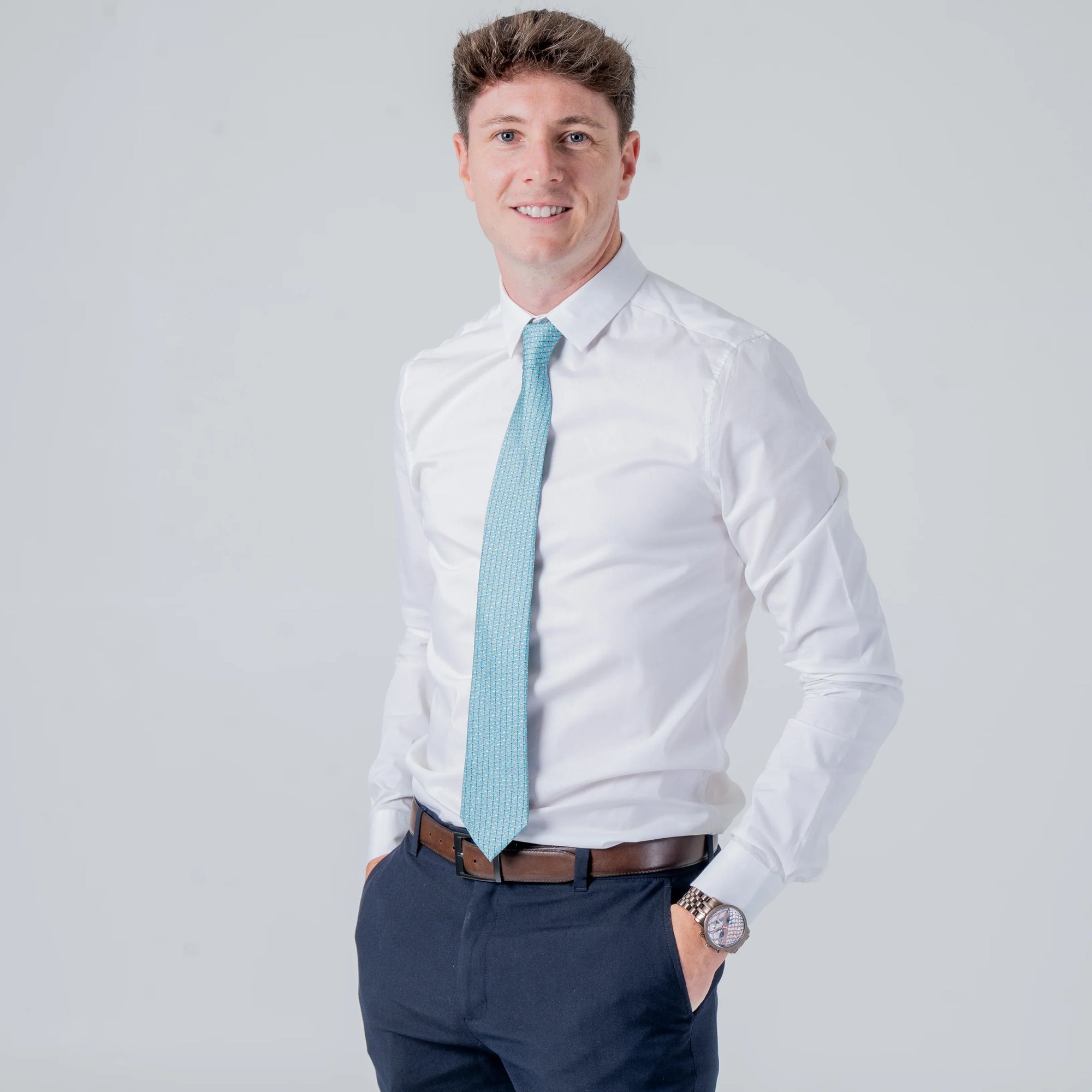 Man wearing Dragonfly Dance - Silk Tie in teal with dragonfly pattern, paired with white shirt and navy pants.