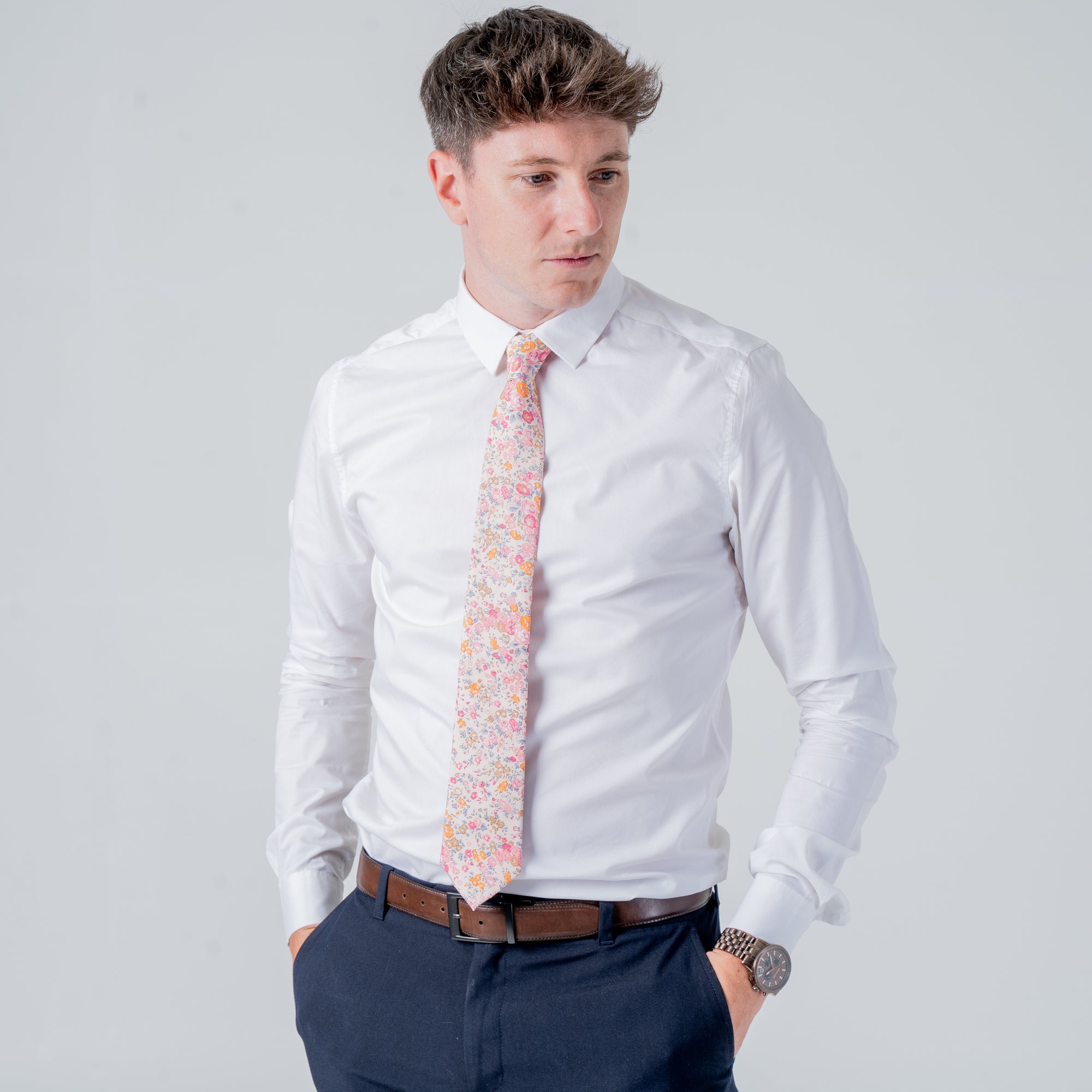Man wearing white shirt and navy pants with a floral patterned Cotswold Bloom - Tie against a plain background
