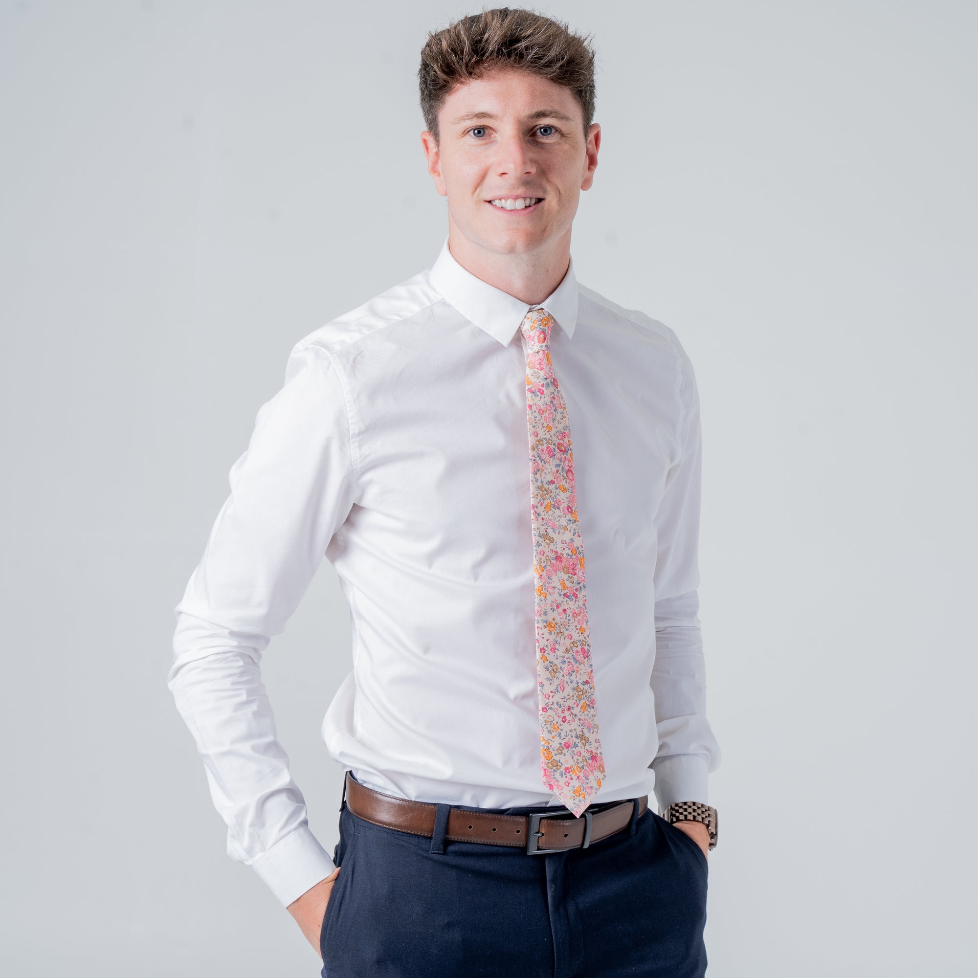 Man wearing a white shirt and Cotswold Bloom tie with floral pattern in pink, orange, and yellow on beige background